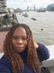 Eucharia looks into the camera. Behind her the Thames is visible and in the distance, Tower Bridge.